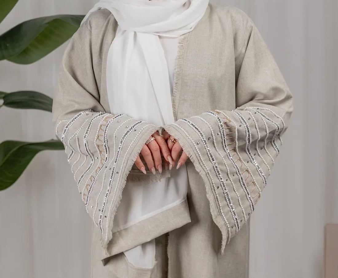 woman wearing a beige outfit with intricate sleeve designs against a neutral background